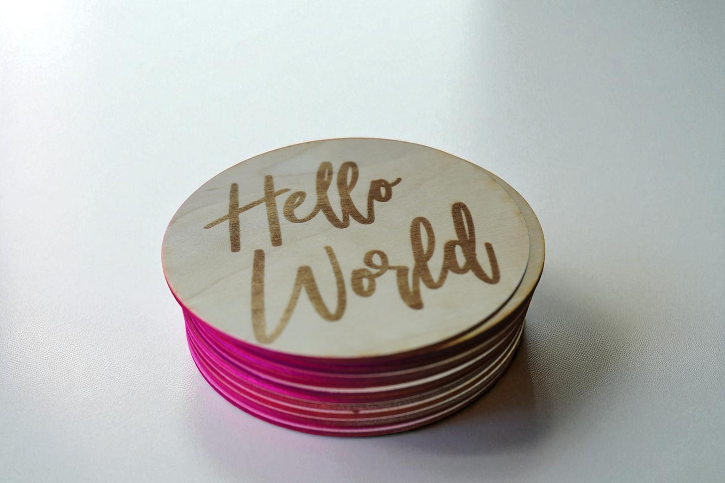 Engraved wooden Hello World baby milestone disc stacked with colorful edge for newborn photo announcements.