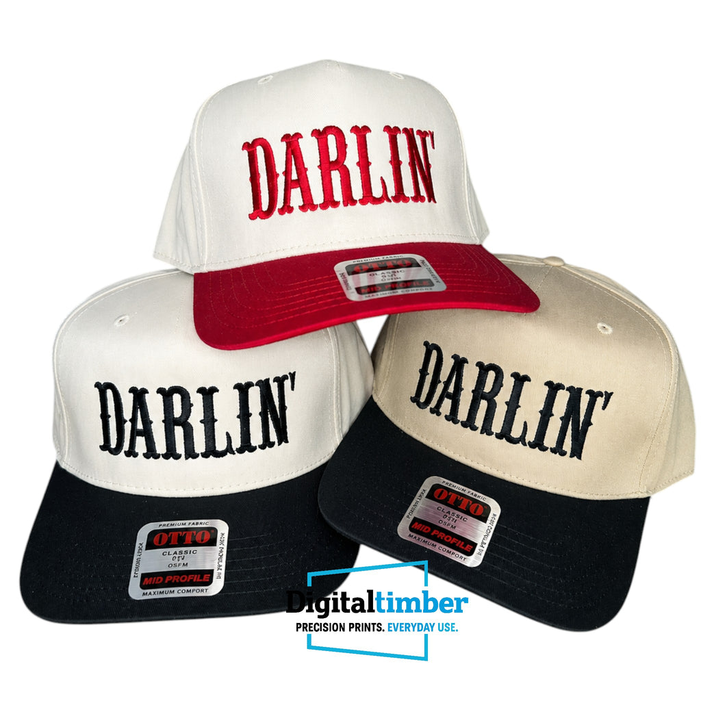 Three snapback hats arranged in a pyramid on a white background. The top hat is white with a red brim and red embroidered 'DARLIN'' text.