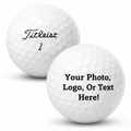 Two white dimpled golf balls on a light gray background. The left ball is printed with the word 'Titleist' in black script and the number '1' below it.