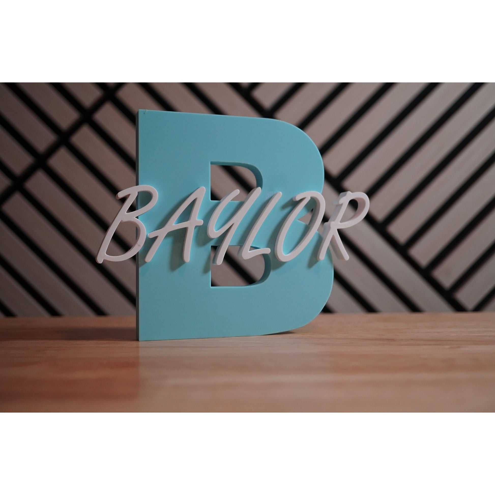Teal letter 'B' with 'Baylor' in white on a wooden surface and patterned wall background
