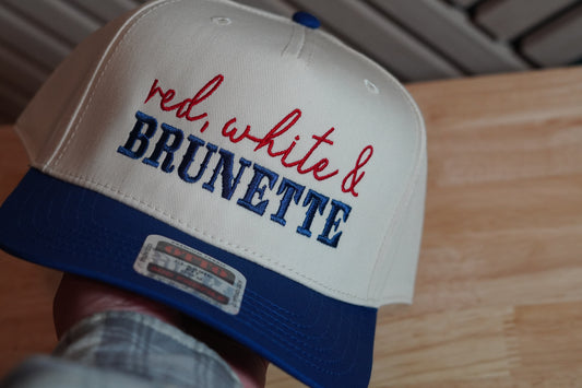 Cap with 'red, white & BRUNETTE' text on a wooden surface