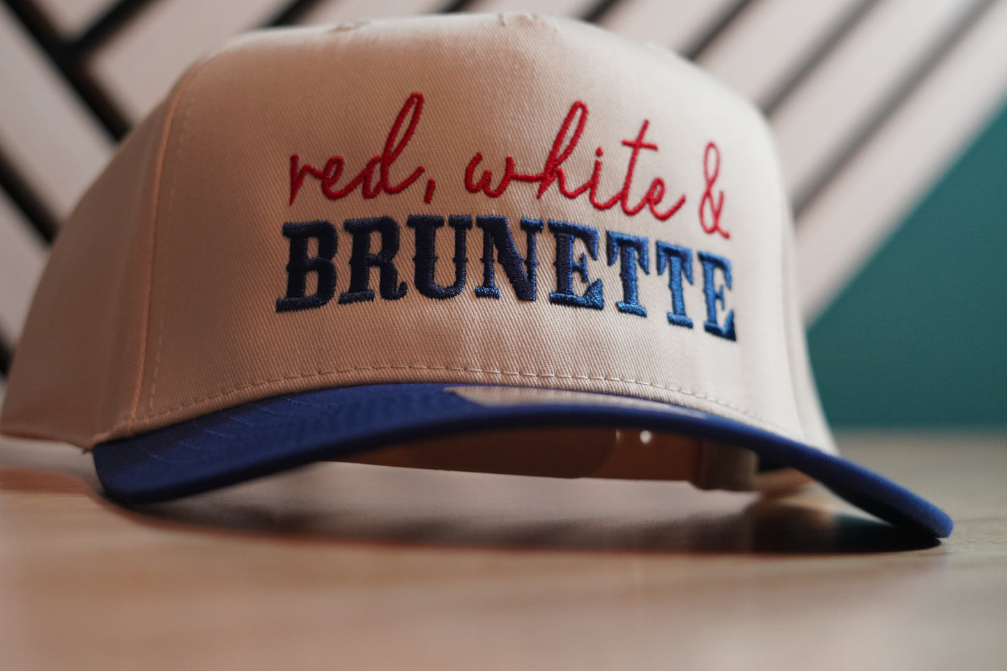 Beige cap with 'red, white & BRUNETTE' text on a wooden surface