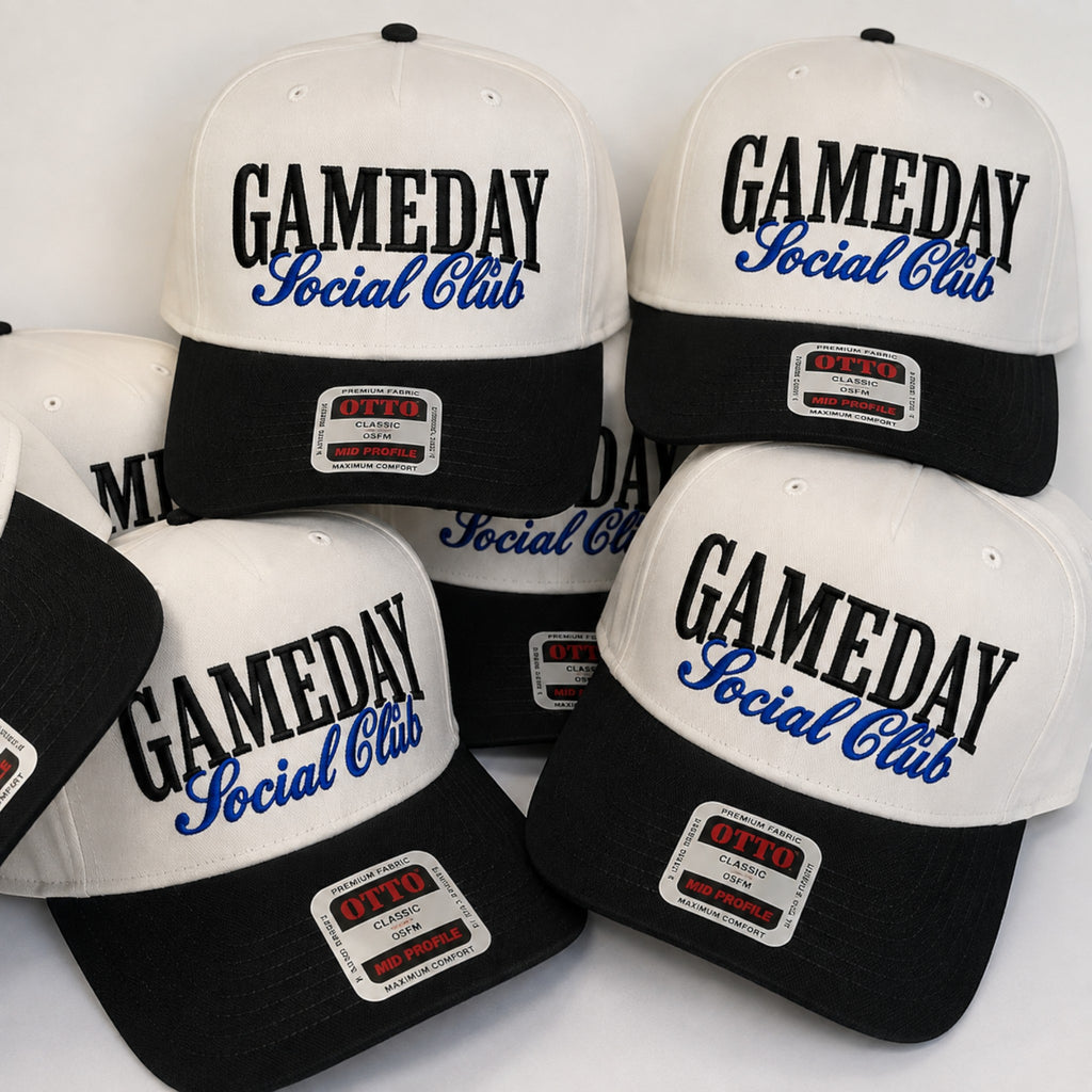 A group of black and white snapback caps with 'GAMEDAY Social Club' printed on the front. The caps feature a white crown, black brim, and a white patch on the brim with 'OTTO' branding.