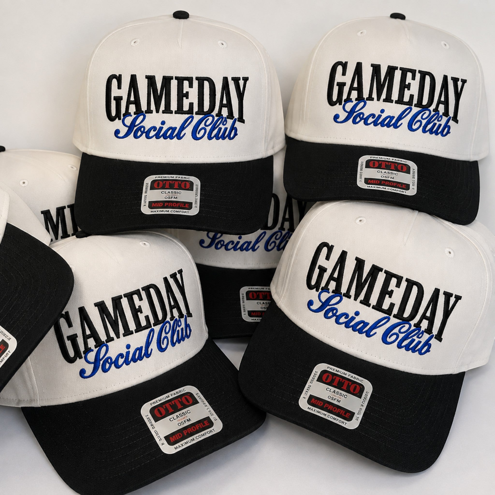 A group of black and white snapback caps with 'GAMEDAY Social Club' printed on the front. The caps feature a white crown, black brim, and a white patch on the brim with 'OTTO' branding.