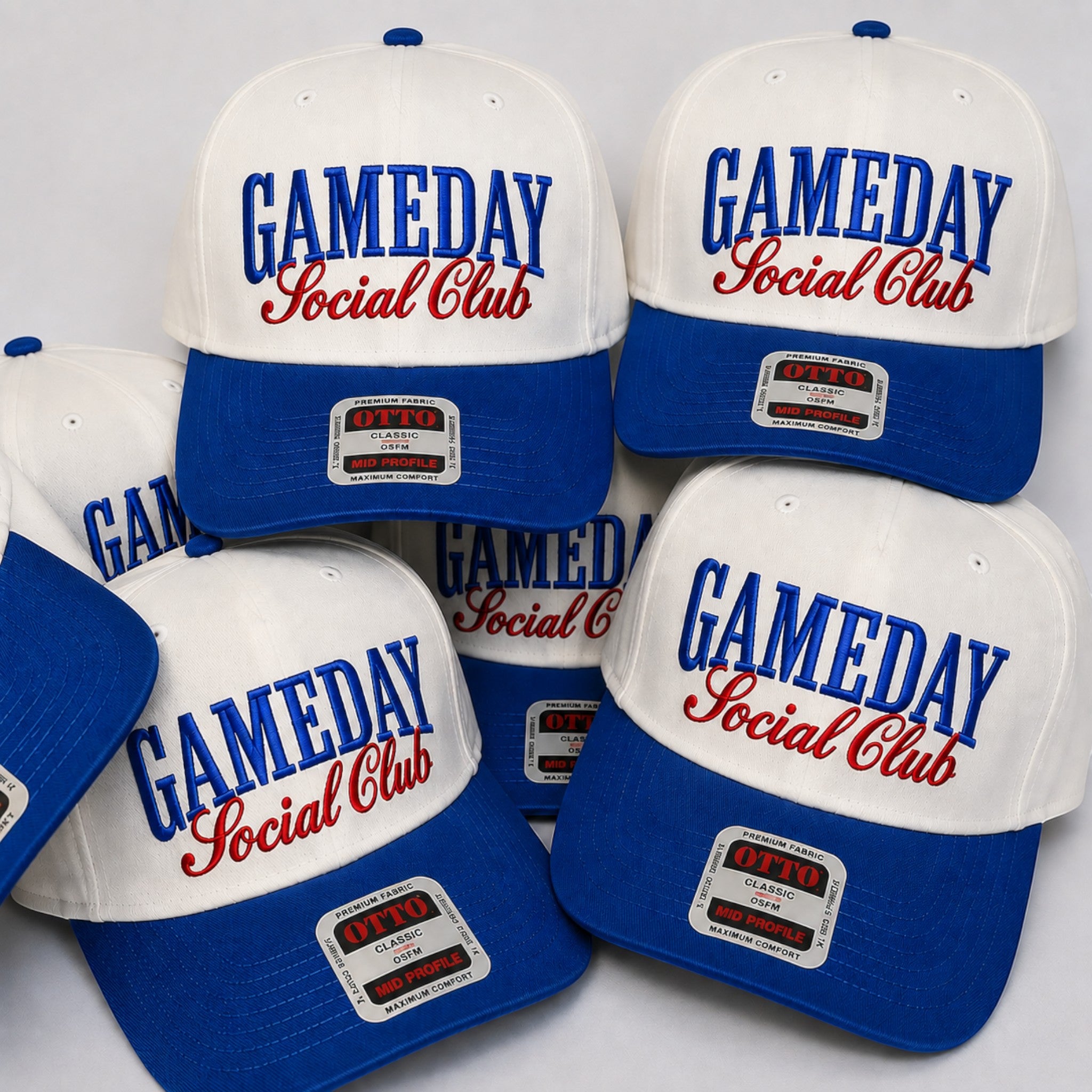 Five white and royal blue baseball caps with 'GAMEDAY Social Club' embroidered on the front, arranged together on a light gray background.