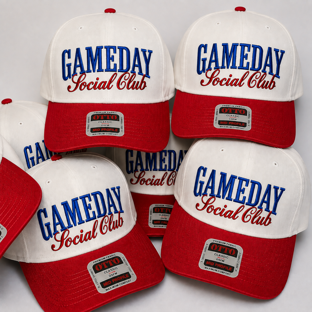 Six white and red baseball caps arranged in a cluster, each embroidered with 'GAMEDAY Social Club' in blue and red script. The caps feature a white crown, red brim, and a silver-toned metal badge on the front of the brim.