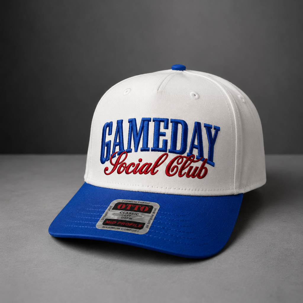 A white and royal blue snapback cap with 'GAMEDAY Social Club' embroidered on the front, photographed on a gray studio background.