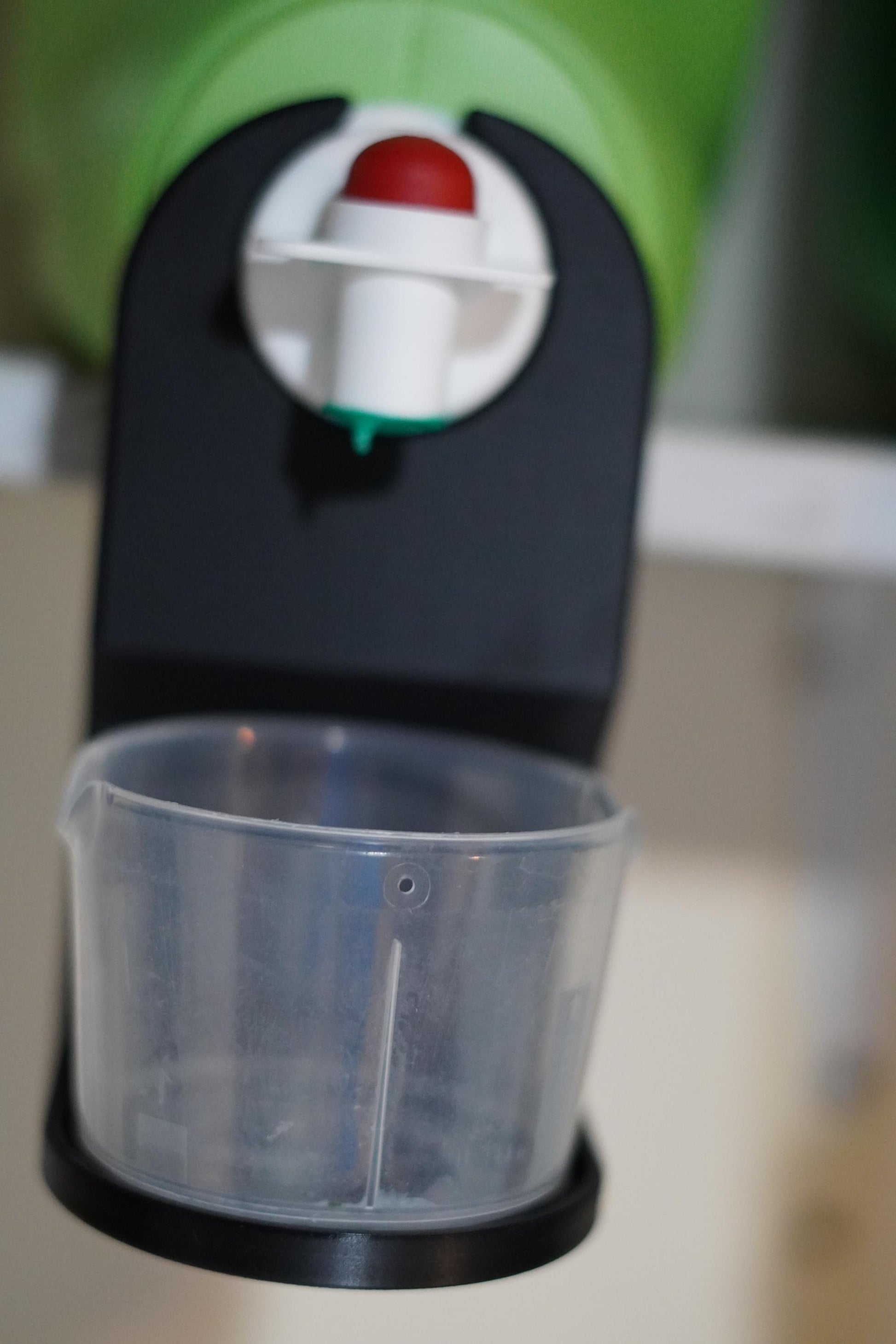 Black drip catcher attachment installed under a large green detergent jug, with clear measuring cup resting in place. (etsy image id: 6784376467)