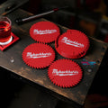Red saw blade coasters with “MyBackHurts” text placed on a dark wood bench with glass of whiskey nearby __etsy:7087228042