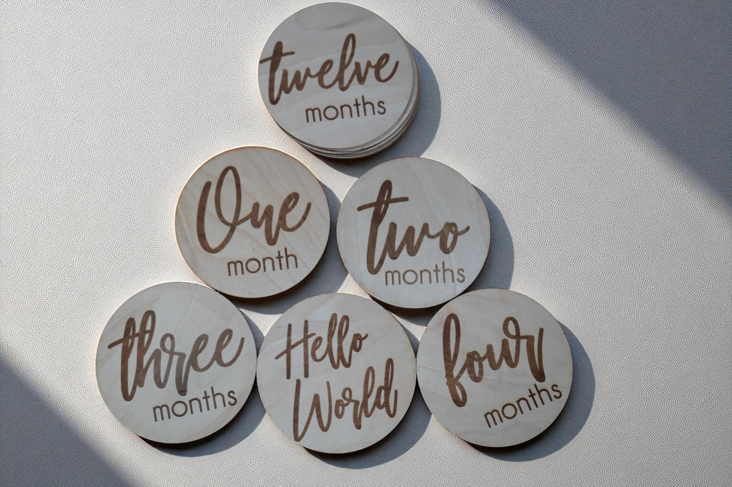 Engraved baby milestone discs in natural wood, featuring one month, two months, three months, and hello world designs. (etsy image id: 7212767948)