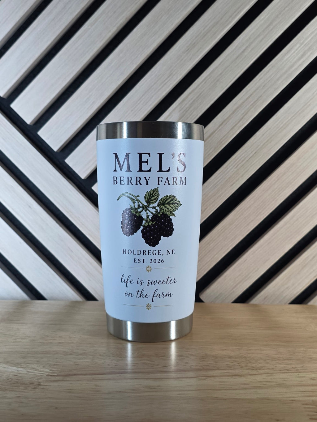White tumbler printed with Mel’s Berry Farm lettering, blackberries, and green leaves.