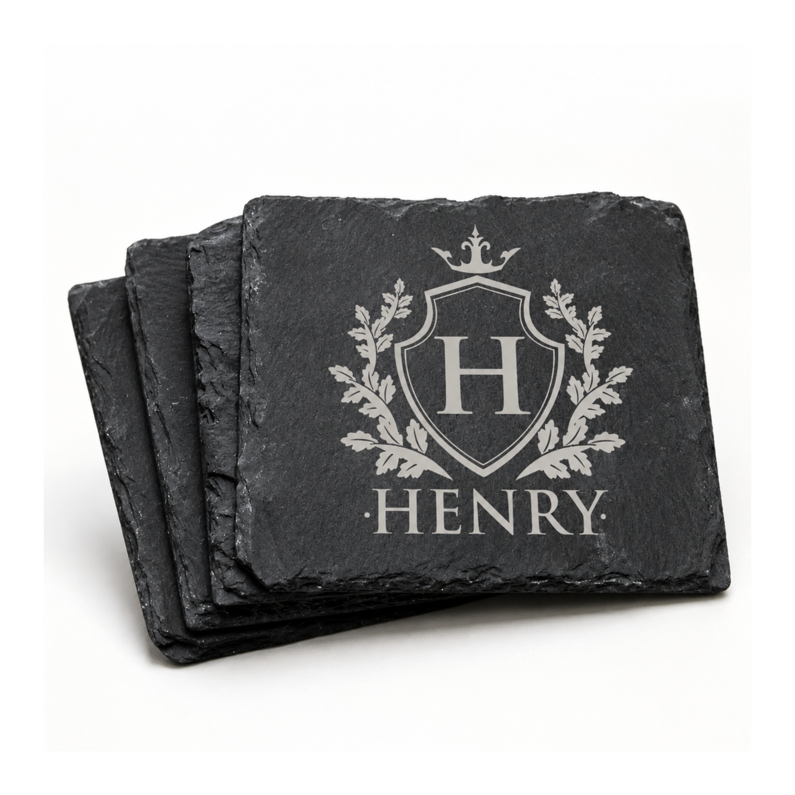 Stack of personalized black slate coasters engraved with a family crest, initial H, and the name Henry.