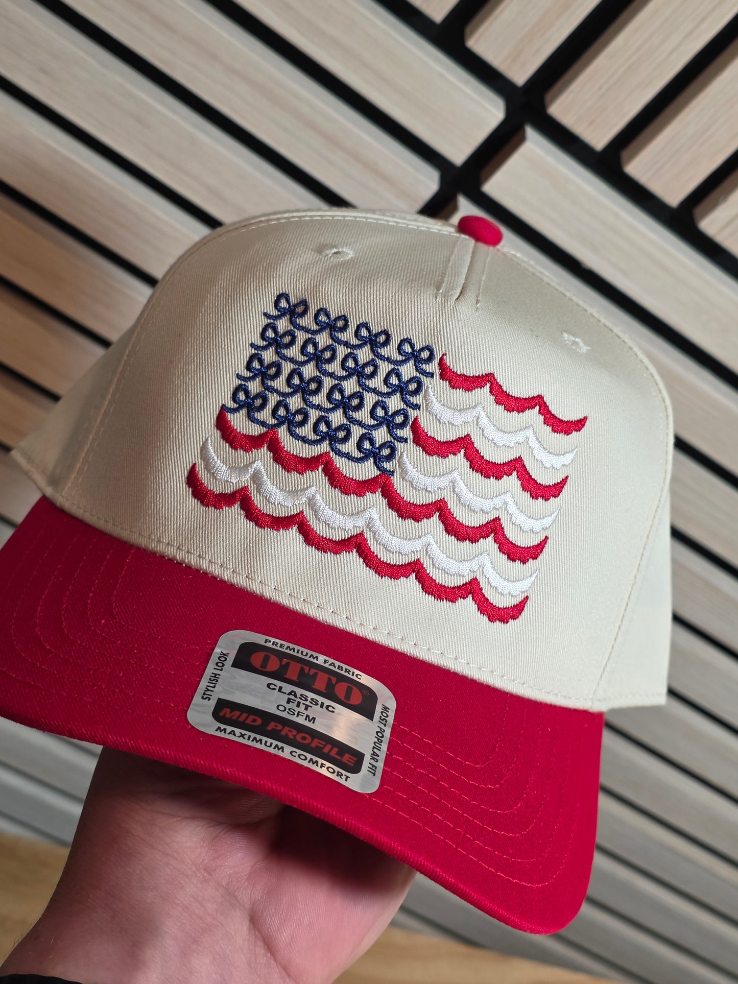 Red and white cap with embroidered design held by a hand on a wooden surface