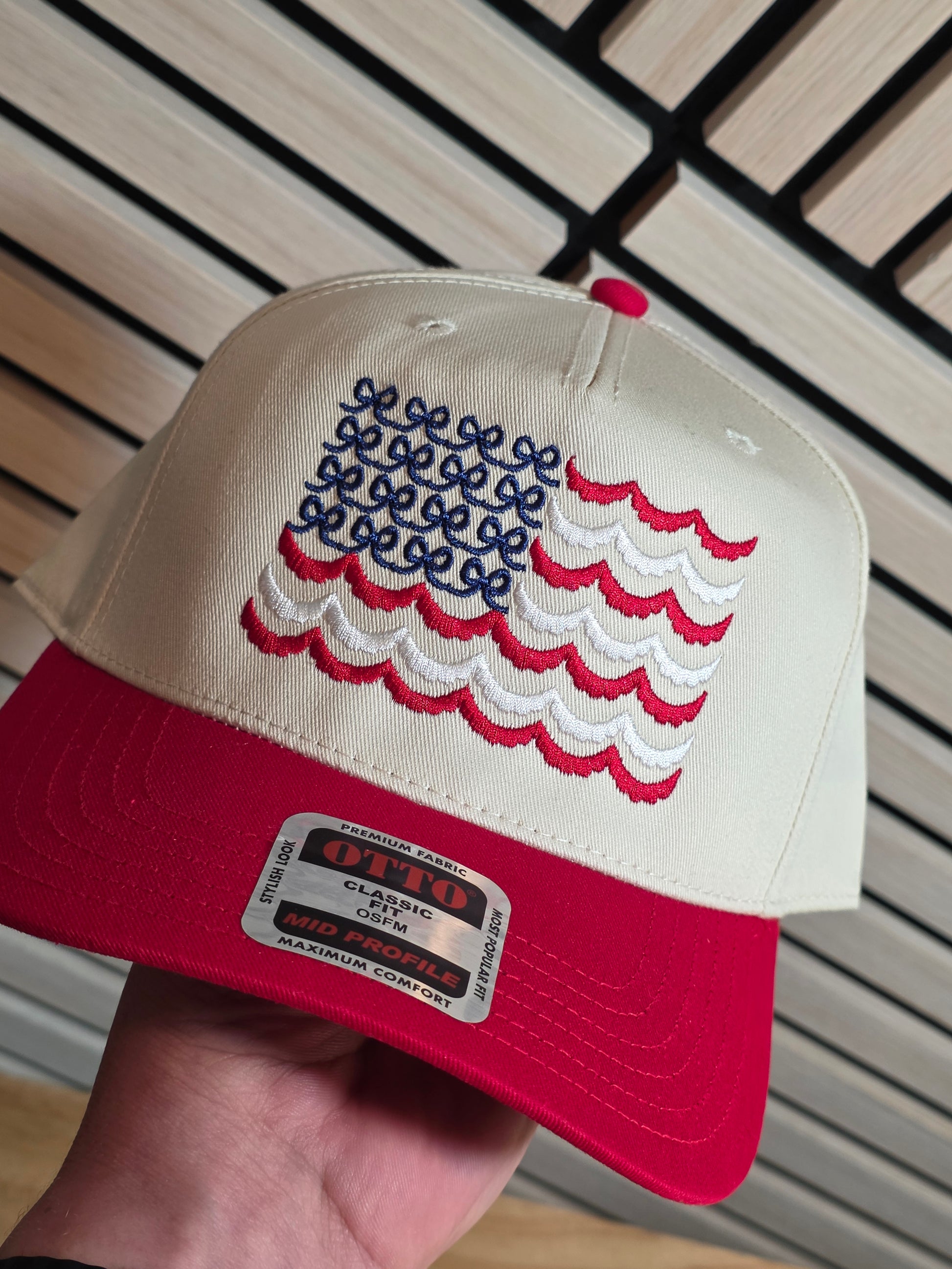 Red and white cap with embroidered design held by a hand on a wooden surface