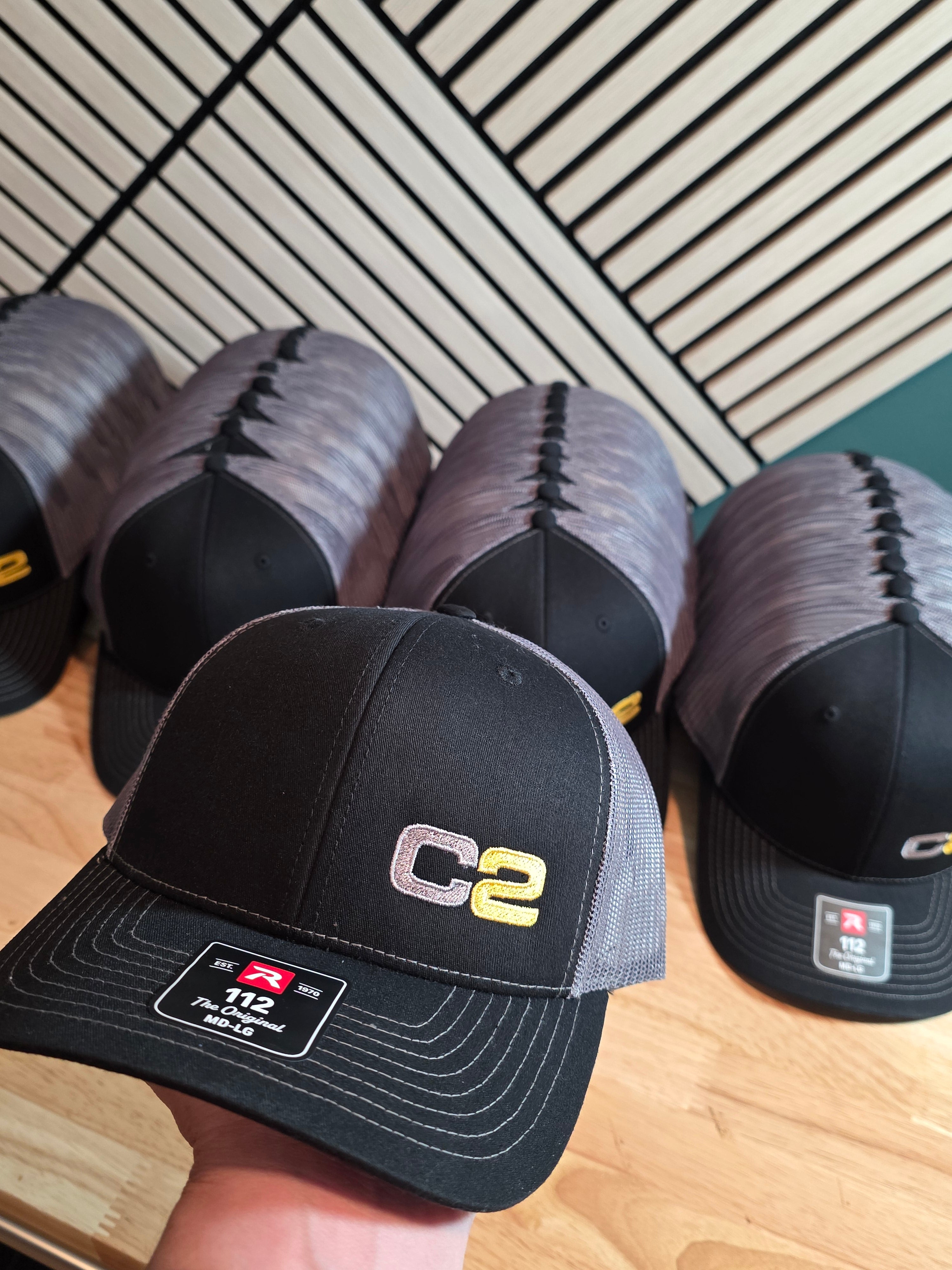 Bulk order of black and charcoal Richardson 112 trucker hats with a two-color embroidered company initials logo, one held up close