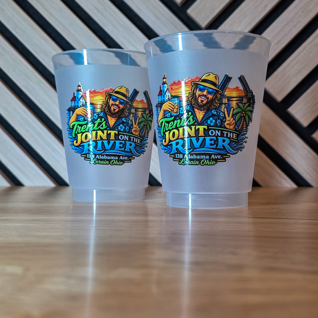 Two frosted clear plastic cups with a colorful 'Frontier's Joint on the River' graphic, displayed on a wooden tabletop against a black and white striped background.