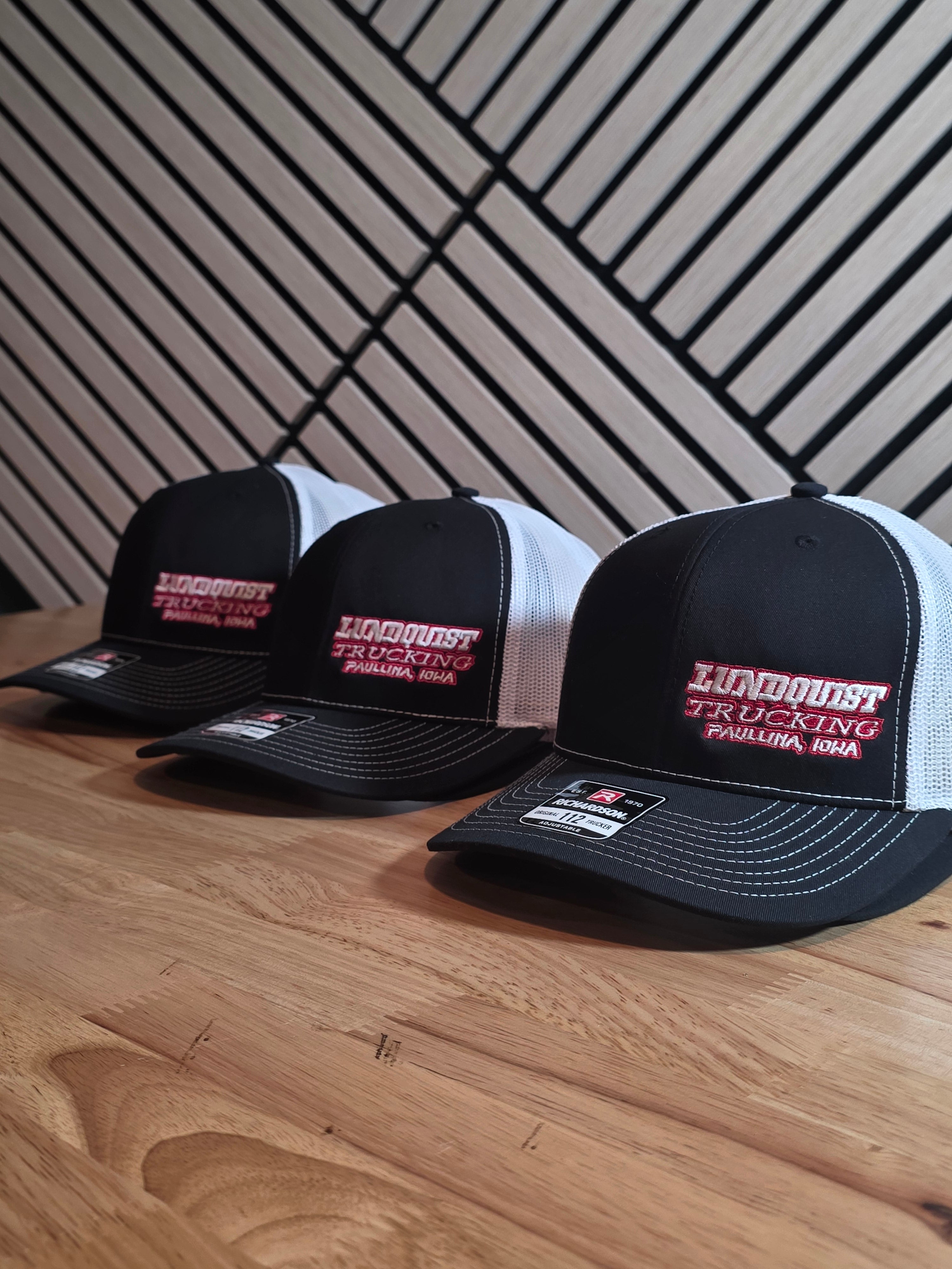 Stacks of navy and charcoal Richardson 112 trucker hats with a green embroidered circular logo, finished bulk embroidery order